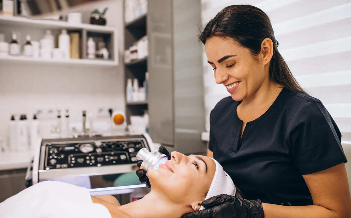 Esteticista sonriente aplicando un tratamiento facial a una clienta en una cabina de estética
