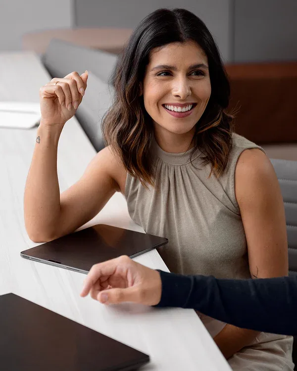 Mujer sonriente en una reunión, con una tableta sobre la mesa